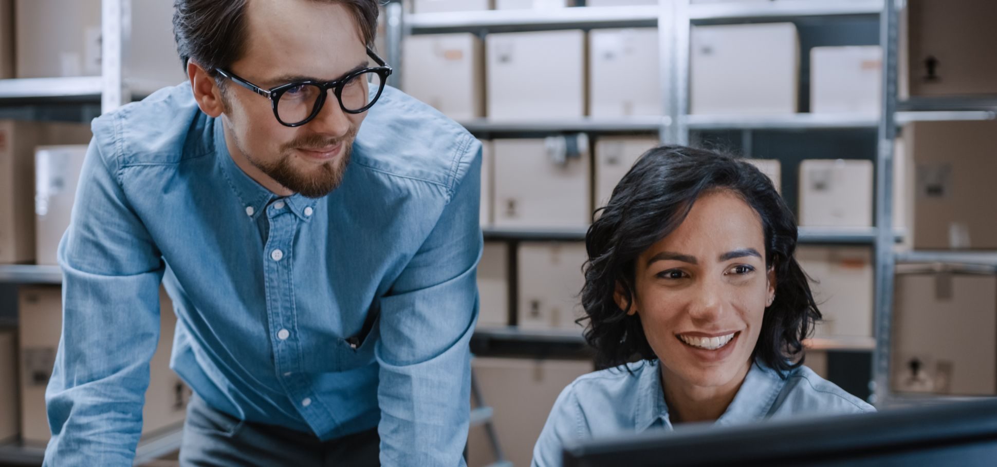 male and female co-workers chat over a laptop in a warehouse