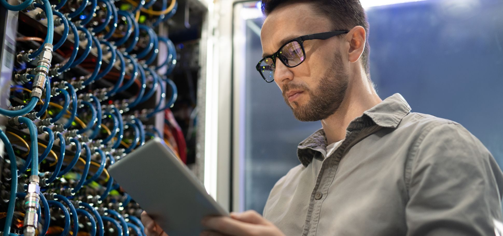 Man wearing glasses works on his tablet in a server room