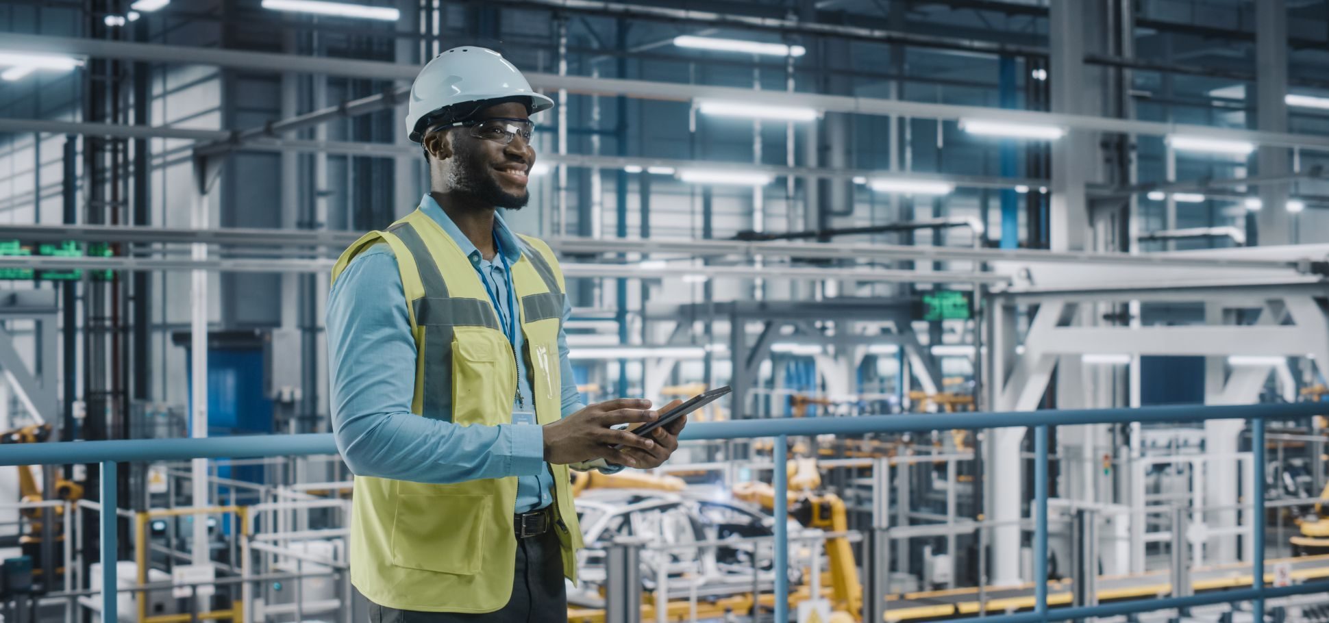 Engineer stands in factory while on laptop